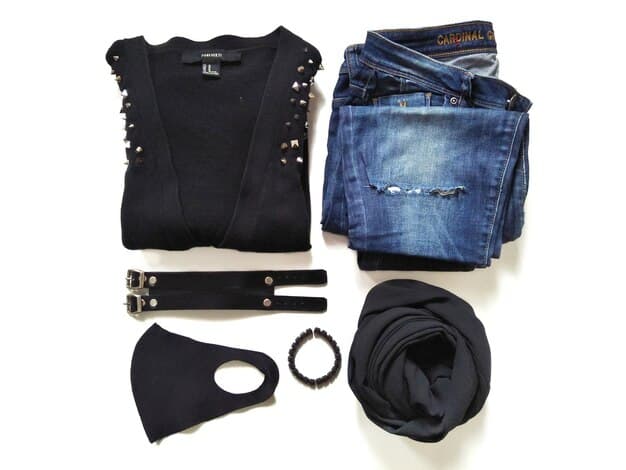 A tightly curated collection of essential wardrobe basics, including a white t-shirt, dark wash jeans, a black blazer, and a little black dress, neatly arranged on a white surface.