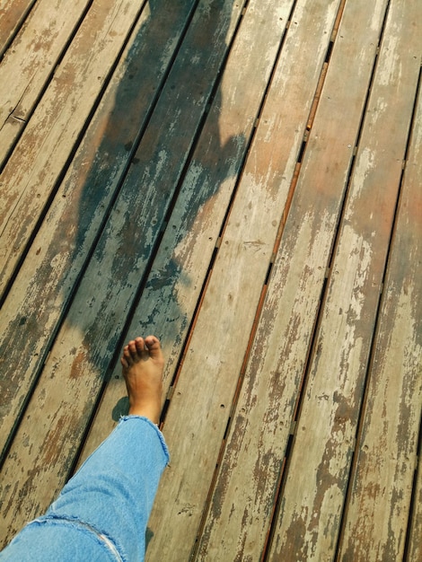 A close-up of a person sanding a wooden pallet outside in bright sunlight. They are wearing gloves and a mask, and there are several other pallets stacked nearby. The focus is on the texture of the wood and the dust being created by the sanding.