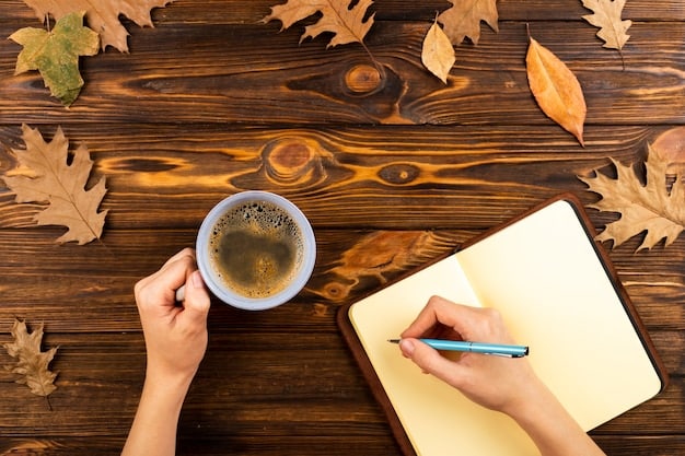 An overhead shot of a person's hands writing in a journal at a wooden desk with a cup of coffee and a plant in the background. The focus is on the journal and pen, with a blurred background that suggests a cozy and productive environment.
