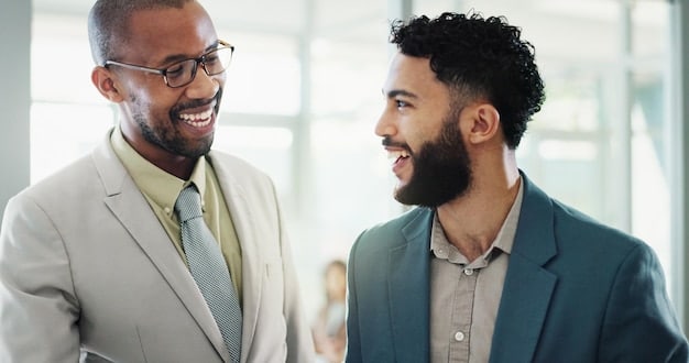 Two colleagues are smiling and nodding during a conversation while maintaining eye contact, showing effective non-verbal communication in a professional setting.