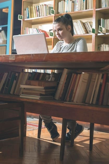 A student studying with books and a laptop in a university library, surrounded by shelves filled with books. Sunlight streaming through the window.